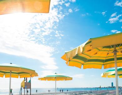 Spiaggia soleggiata con ombrelloni gialli, cielo azzurro e mare sereno.