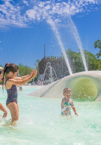 Famiglia si diverte in piscina con spruzzi d'acqua e sole splendente.