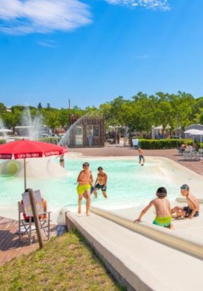 Piscina con scivoli, bambini giocano sotto il sole estivo.