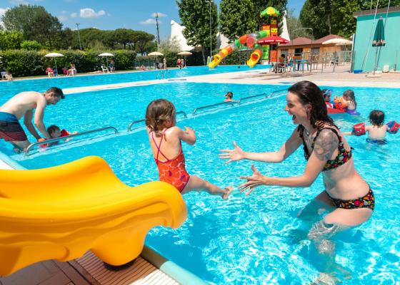 Kinder spielen im Pool mit gelber Rutsche und Erwachsenen.