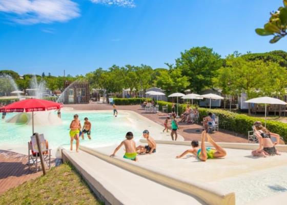 Piscina con scivoli, bambini giocano sotto il sole estivo.