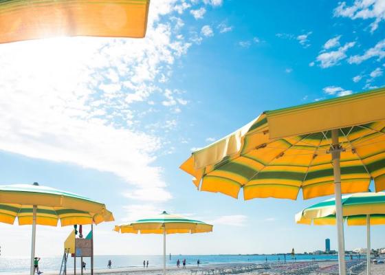 Spiaggia soleggiata con ombrelloni gialli, cielo azzurro e mare sereno.